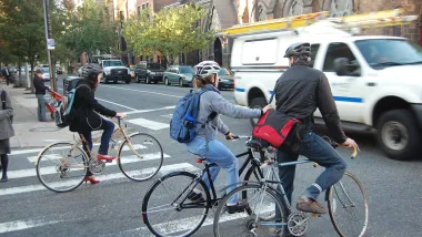 People on bike wearing helmets stopped at intersection waiting for passing cars in Philadelphia, Pennsylvania.